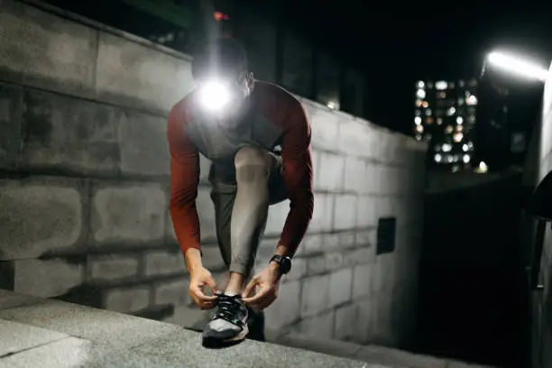 Handsome young man with headlamp tying his shoes before running at night