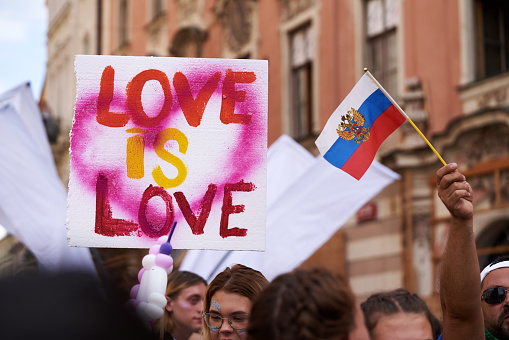 Prague, Czech Republic - August 13, 2022: Placard saying Love is love about peoples' heads at gay pride, with Russian flag