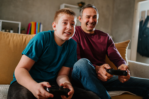 Close up shot of a tense young blond boy playing a video game against his happy father. Focus on young boy's facial expression and his desire to win the game. Special family moments of enjoyment.