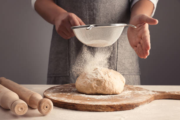 istock Man sprinkling flour over dough at table near grey wall, closeup 1486168645