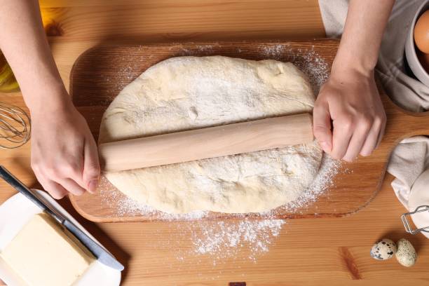 istock Woman rolling dough with wooden pin at table, top view 1486168659
