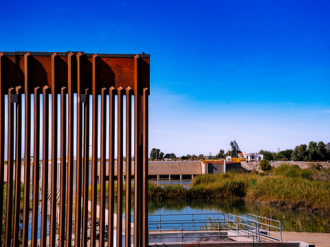 A towering barrier of steel and concrete stretches across the dusty, desert landscape, dividing the United States from Mexico and symbolizing the complex, controversial issues of immigration and border security.