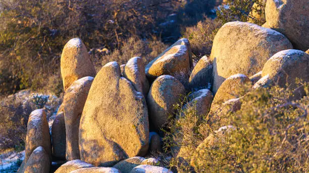 A large grouping of granite rocks with snow-covered tops during winter in Joshua Tree National Park, California.