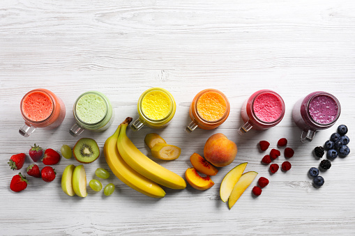 Many different tasty smoothies and ingredients on white wooden table, flat lay. Space for text