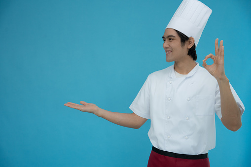 Portrait of a handsome Asian man wearing chef clothes on blue isolated background. Chef smiles and is happy with the food that is ok with the presentation.