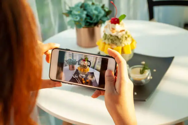 Photo of An Asian woman takes a picture of an ice-mango in a cafe and prepares to upload it to a social app.