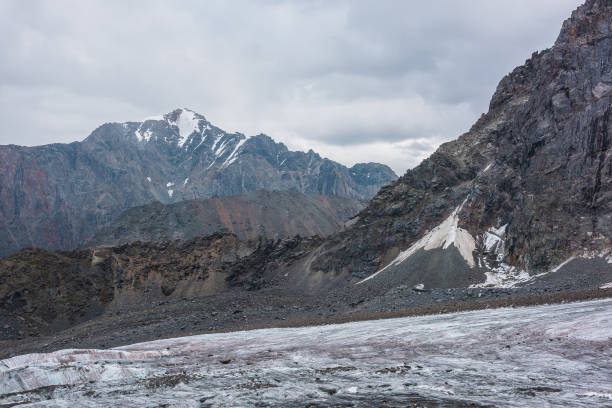 istock Awesome landscape with long glacier tongue against high mountain range with sharp rocky peaked top in overcast weather. Cone shaped pointy peak in dramatic cloudy sky. Large glacier among sharp rocks. 1486178496