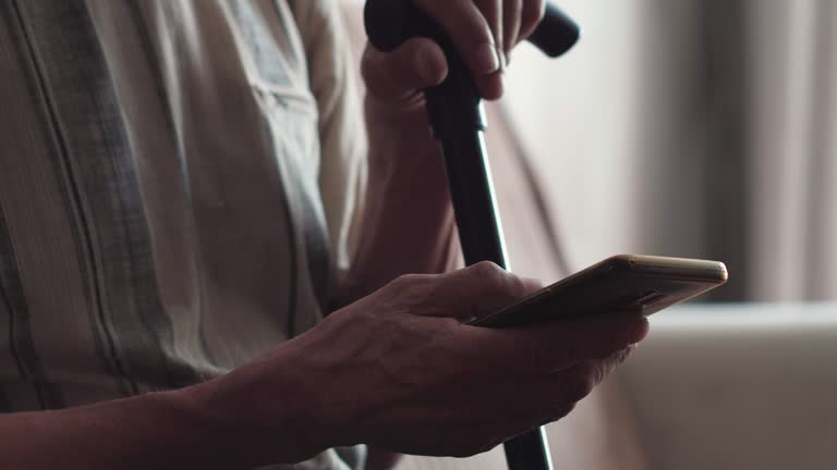 a pensioner with a walking stick while sitting uses a smartphone, mobile applications, the Internet, social networks while inside.lifestyle of a modern pensioner