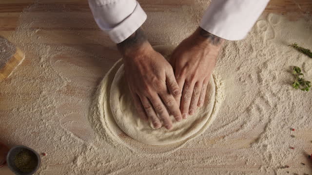 Pastry cook hands kneading raw bread dough on restaurant kitchen cutting board.