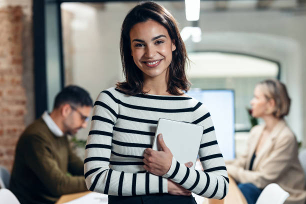 istock Attractive young designer woman working with digital tablet while looking at camera in a modern office at home. 1486181449