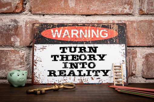 Turn Theory Into Reality. Warning sign on wooden texture office desk.