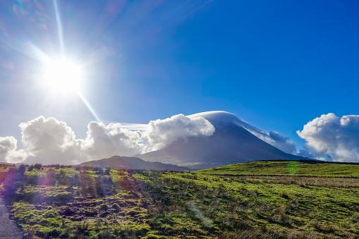 Fluffy white clouds blanket Mount Pico in the Azores, shielding it from the bright morning sun.