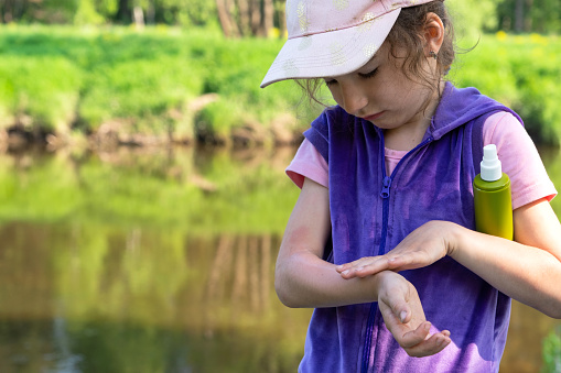 Girl sprays mosquito spray on the skin in nature that bite her hands and feet. Protection from insect bites, repellent safe for children. Outdoor recreation, against allergies. Summer time