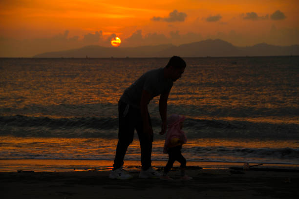 A father playing with his children on the beach in Kampung Jawa, Banda Aceh, Indonesia. against the background of the sunset 04/09/2021