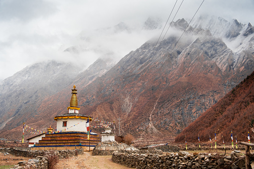 A picturesque landscape with a Buddhist pagoda for prayers surrounded by high snow-capped mountains, sharp peaks are covered with thick fog and low clouds