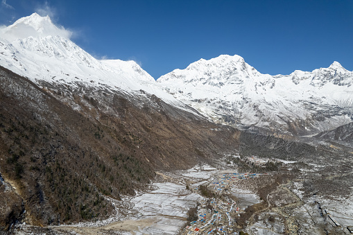 The peaks of the snow-capped mountains of Nepal surround a small village with low-rise buildings with colored roofs