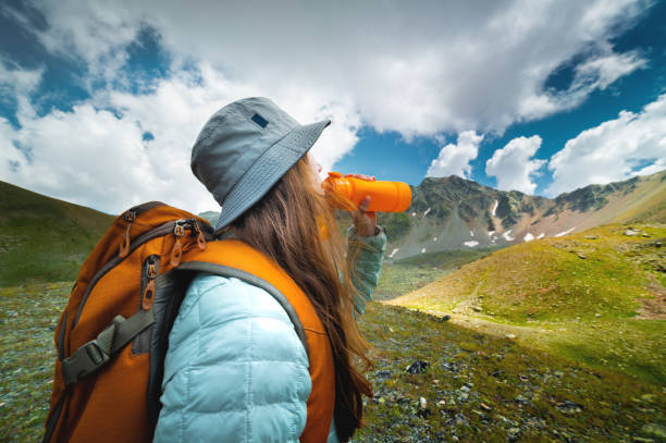 woman takes a break to drink from a water bottle while hiking. Young hiker drinks water in a mountain valley stock photo