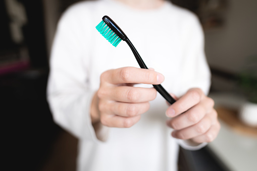 A woman's hand with a black and green toothbrush on a white background pulls a clean empty brush into the frame, a girl without a face.