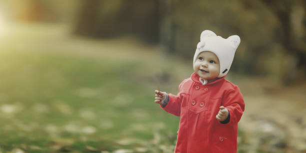 Charming one years old thoughtful baby in red coat enjoying nice and sunny autumn day in park, looking up away. Portrait of little pensive toddler in fall forest. Childhood concept. Copy ad text space encantador bebé pensativo de un año con abrigo rojo disfrutando de un agradable y soleado día de otoño en el parque, mirando hacia otro lado. retrato de un pequeño niño pensativo en el bosque de otoño. concepto de infancia. copiar el espacio de text