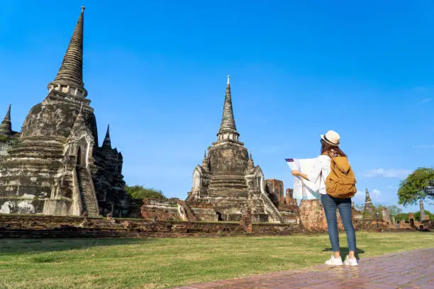 young solo woman backpacker using paper map guide while traveling to Wat Phra Si Sanphet in Ayutthaya historical park Pagoda ancient temple, UNESCO attractive famous place during holiday vacation