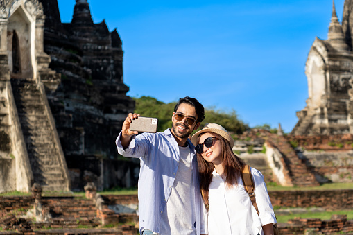 young foreign couple tourist taking selfie photo or making video call at Wat Phra Si Sanphet in Ayutthaya historical park, UNESCO attractive pagoda ancient temple while traveling on holiday vacation