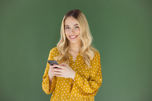 Beautiful blonde woman on green background using smart phone.