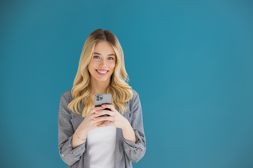 Beautiful blonde woman on blue background using smart phone.