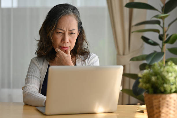 pensativa y confundida dama de negocios de mediana edad de los años 60 preocupada pensando en el trabajo en línea, el trabajo remoto desde casa. - portrait senior adult confusion women fotografías e imágenes de stock