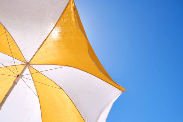 ombrello giallo e bianco su un cielo blu per proteggersi dal sole sulla spiaggia - parasol umbrella sun beach foto e immagini stock