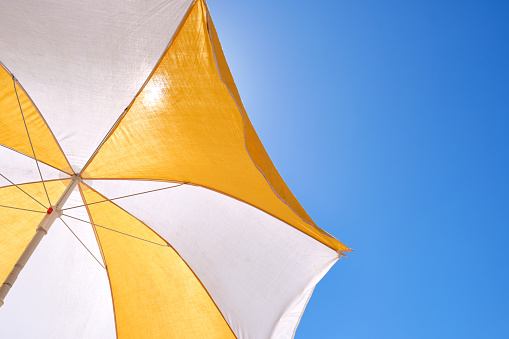 yellow and white umbrella on a blue sky for protection from the sun on the beach