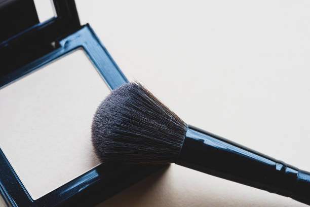 istock Makeup brush picking up compact face powder close-up. Decorative cosmetics on a beige background. Makeup artist workflow. 1486229340