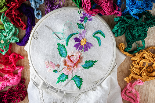 embroidery hoop with floral embroidery. floss threads around. top view.