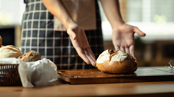 Male baker holding baked sourdough bread. Healthy eating and traditional bakery and pastry concept.