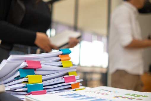 Businesswoman hands working on stacks of paper documents to search and review documents piled on table before sending them to board of directors to use  correct documents in meeting with Businessman