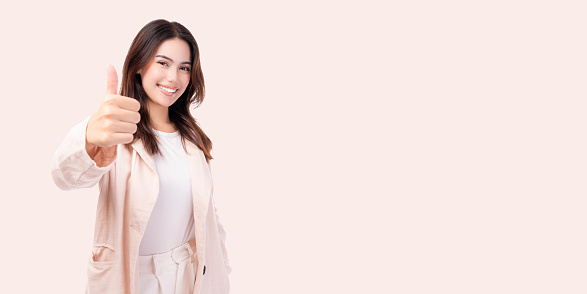 Smiling young business woman showing thumbs up isolated on pink background studio Young happy fun asian girl looking at camera show thumb up gesture with smile face Beautiful lady feeling happiness