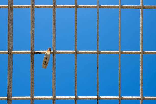 Detail of a white rusted fence with a rusted padlock. Bright blue sky in the background. Marsala, Sicily, Italy.
