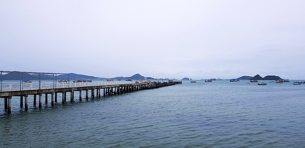 Long bridge among sea or ocean with many boat and white sky background at port Phuket, Thailand. Seascape view with mountain and Natural with