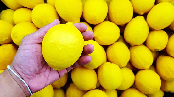 Close up hand of person holding lemon with copy space. Selection and Choice for buy best food, vegetable or fruit at market or supermarket.