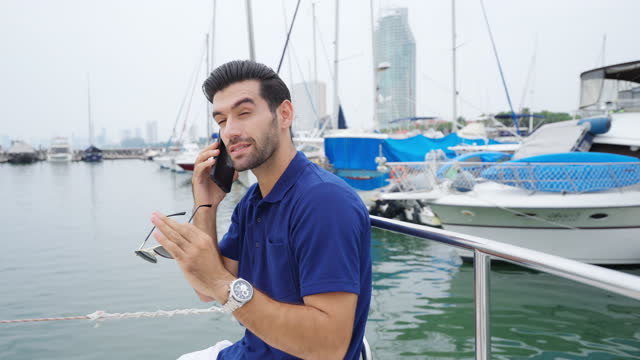 4K Caucasian businessman talking on mobile phone while travel on luxury yacht sailing in the ocean.