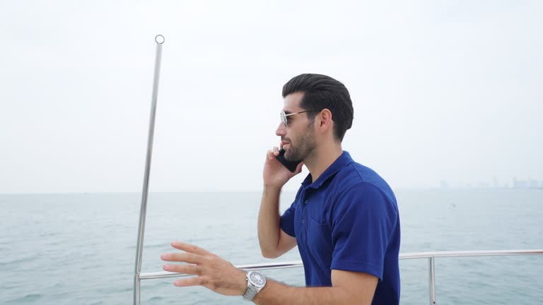 4K Caucasian businessman talking on mobile phone while travel on luxury yacht sailing in the ocean.