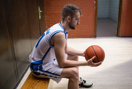 Closeup basketball player wearing orange sportswear, holding ball isolated on white background, selective focus. Sport concept