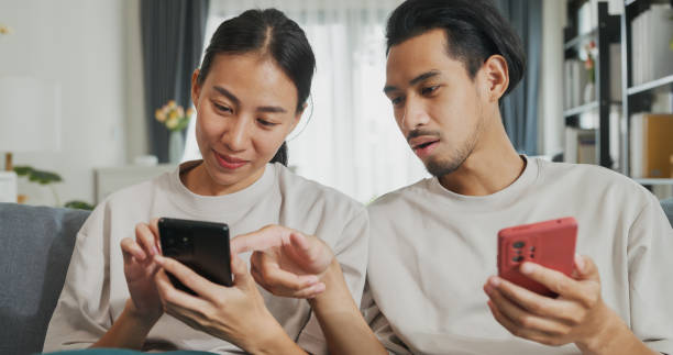istock Young Asian couple sit on couch spend time together have fun use smartphone devices online shopping at home. Happy Young husband and wife laugh relax with phone, Lifestyle domestic activity. 1486256330