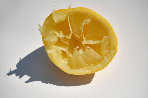 Half of a squeezed lemon against a white background in strong contrasty bright light.