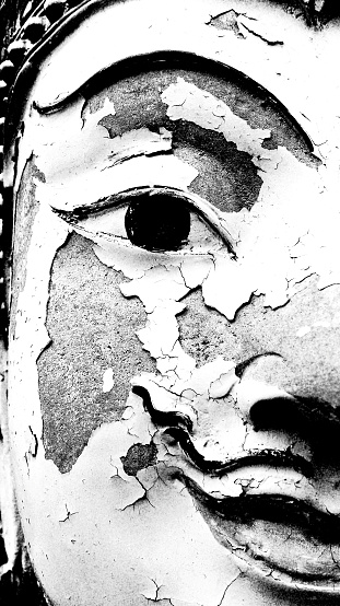 Close up half face of stone Buddha statue broken, injured or damaged in black and white style at temple. Art and Religion in monochrome tone concept