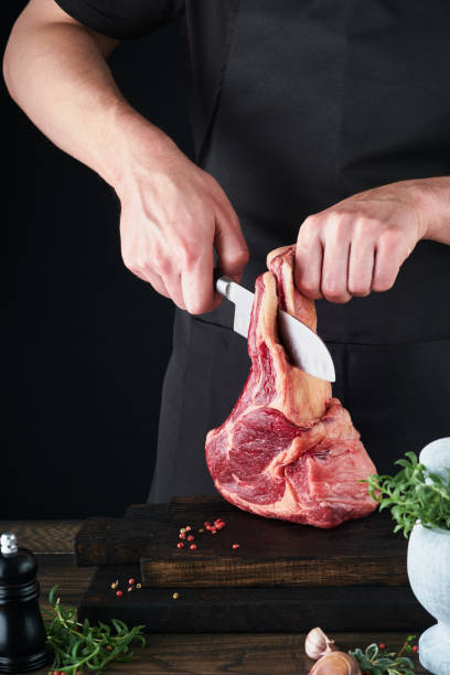 istock Chef cutting steak beef. Mans hands hold raw steak Tomahawk on rustic wooden cutting board on black background. Cooking, recipes and eating concept. Selective focus. 1486271916