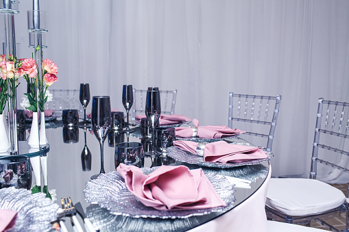 Stylish banquet table setting. Mirrored table, dark glasses, silver plates, purple napkins.