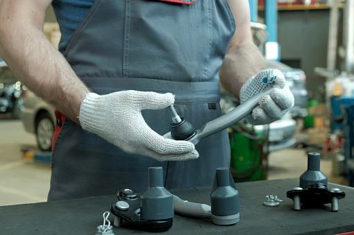 The car mechanic holds the steering tip to control the suspension of the car. Checking the spare part before installation.