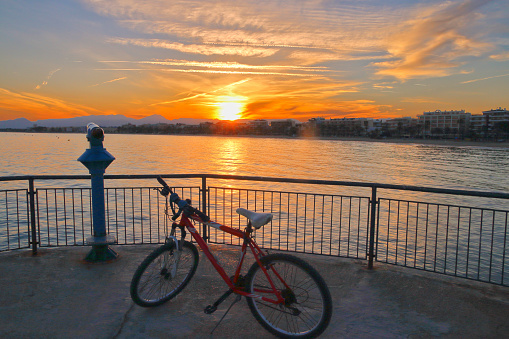The picture was taken in Spain, on the edge of the marina in the town of Salou. In the photo seen a bicycle on the viewing platform. In the distance can be seen the sunset sea and mountains.