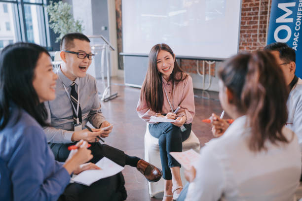 istock Team building Asian workshop participants in small group laughing during discussion, brainstorming during business workshop class 1486286622