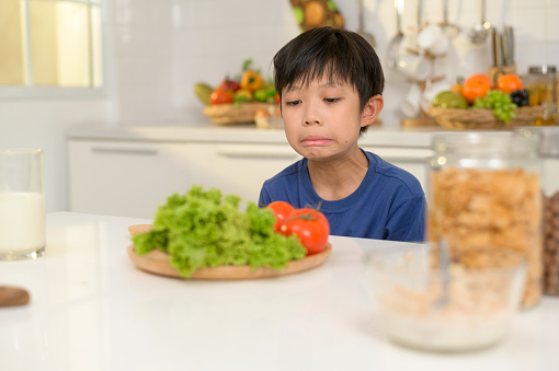 Asian boy feeling bored , unhappy to eat vegetables , health care concept